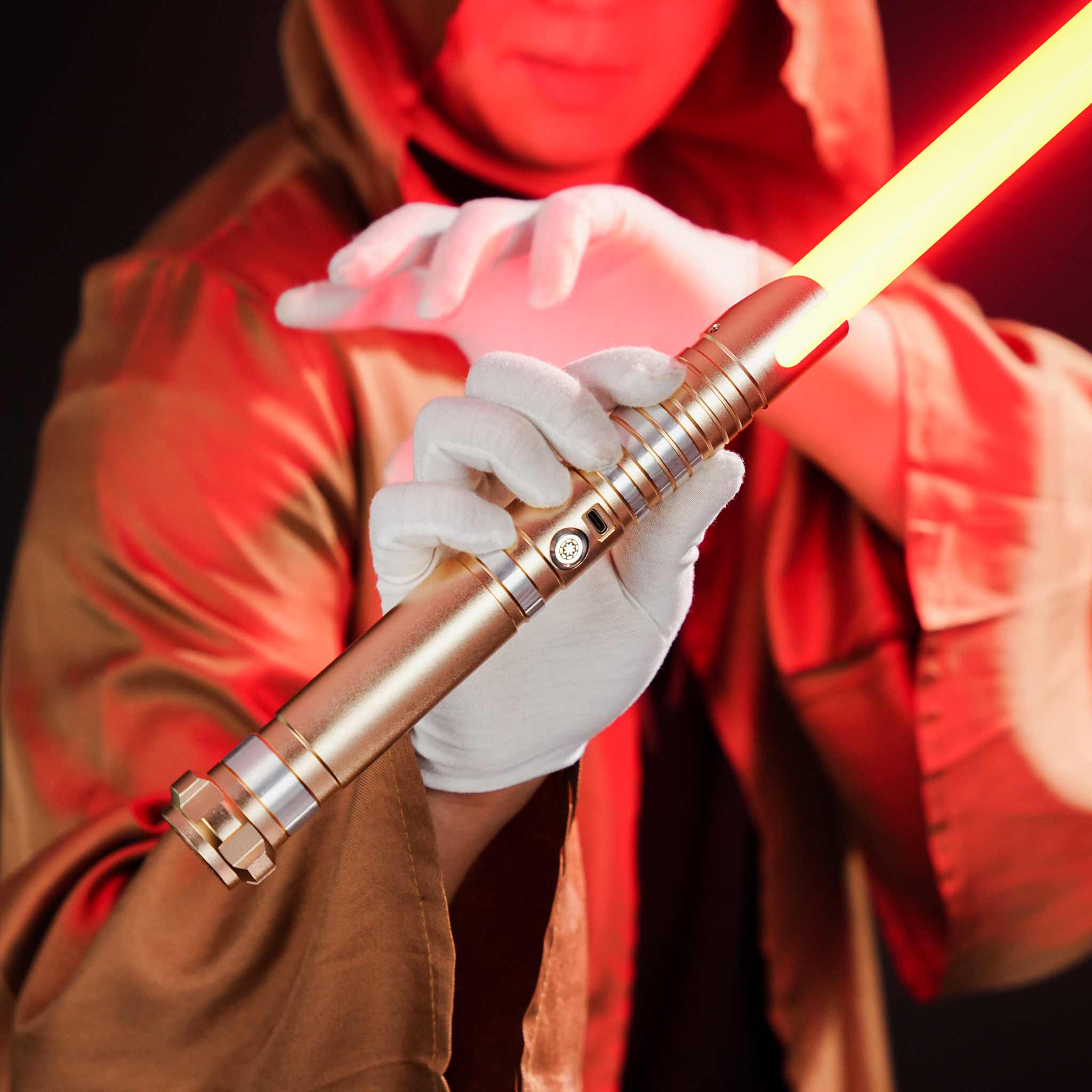 Cosplayer in a red robe holding a gold metal lightsaber hilt in hands with white gloves